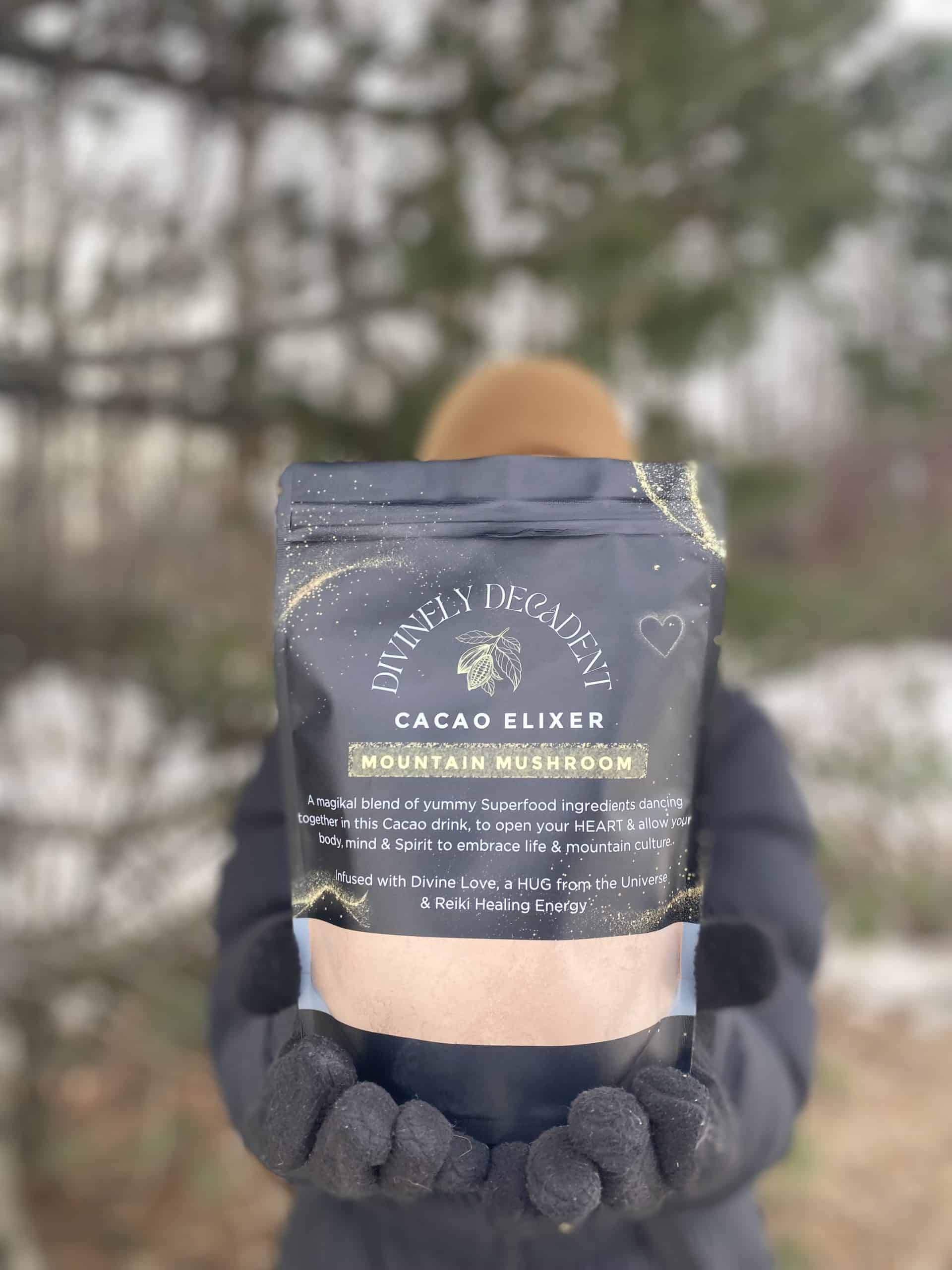 Hands in mittens hold up a bag of Divinely Decadent Cocao Elixir powder, a light brown colour.